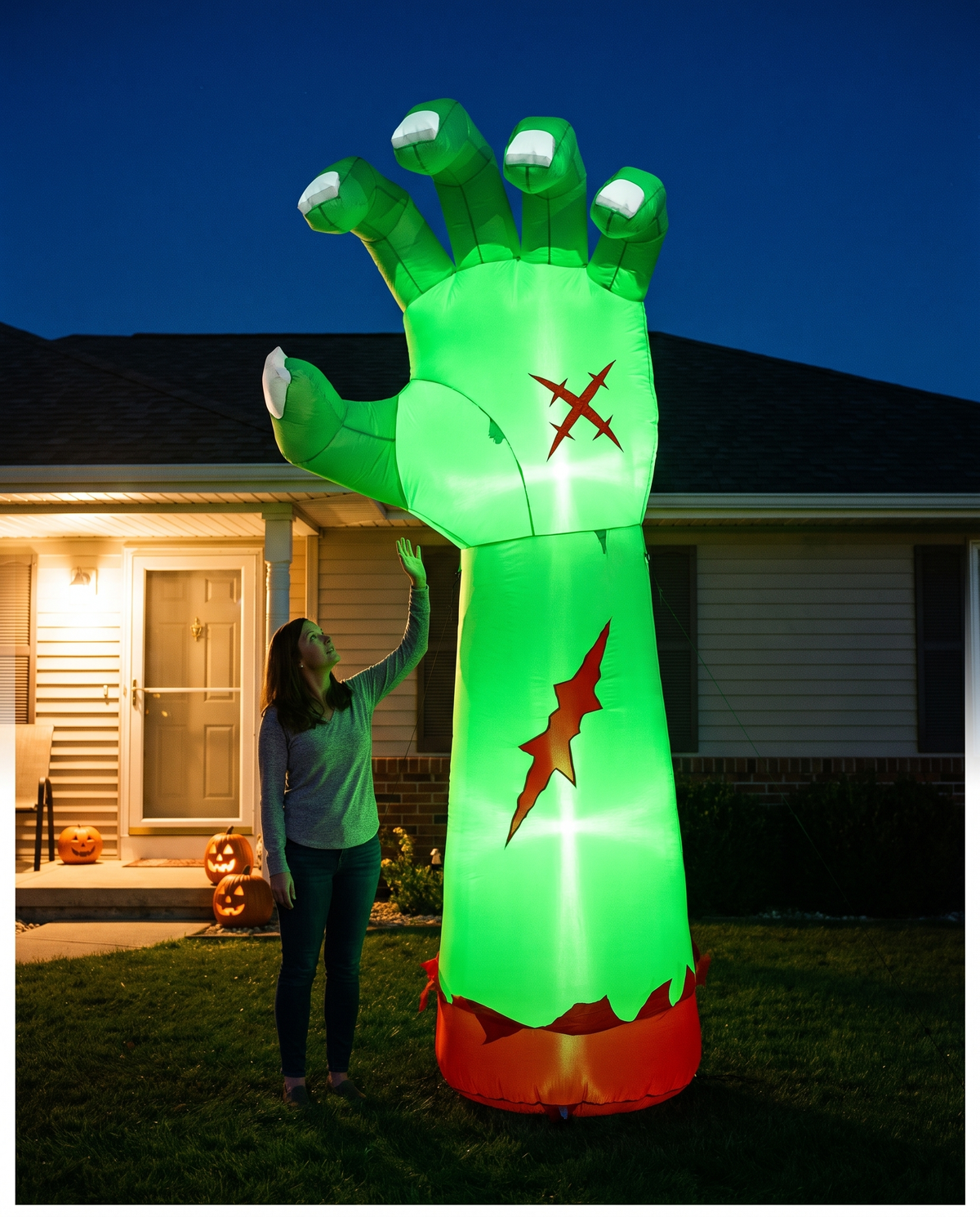 Nine foot tall green inflatable zombie arm glowing on a front lawn at night, towering above an adult standing beside it